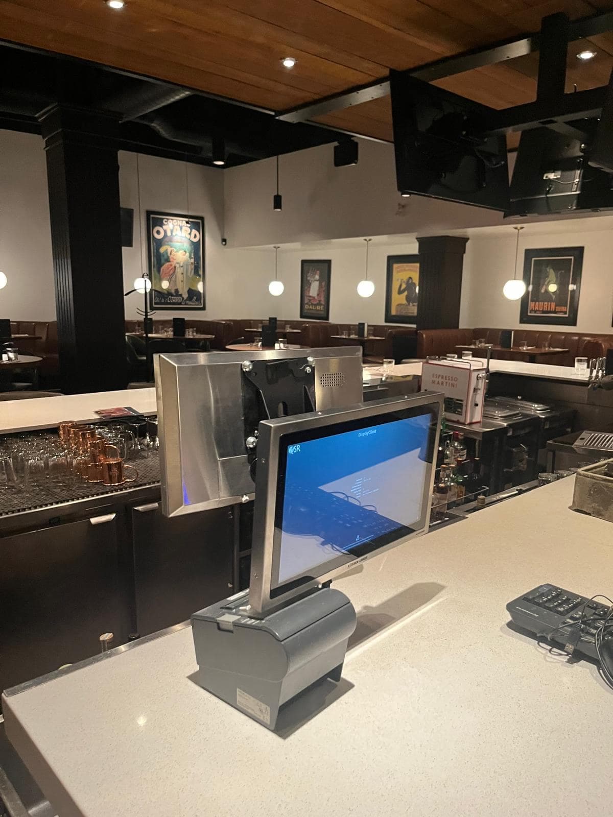 Point-of-sale screen and receipt printer on a bar counter in a restaurant dining room