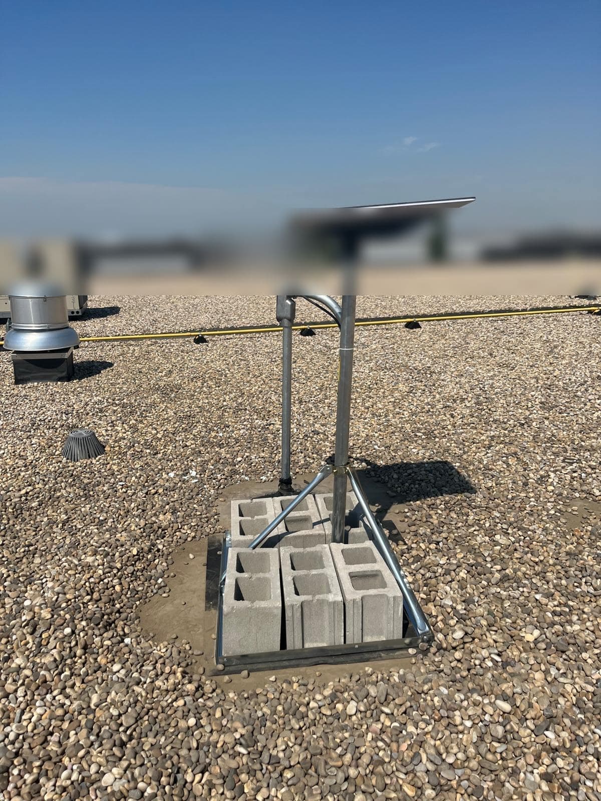Starlink dish on a ballasted tripod on a gravel commercial roof with a neighbouring warehouse in the background