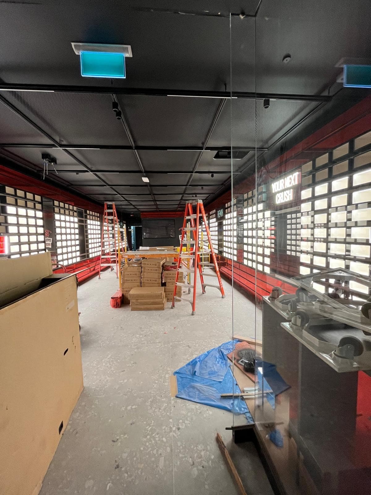 Retail store interior mid-fit-out with stepladders, backlit display walls and ceiling-mounted AV equipment