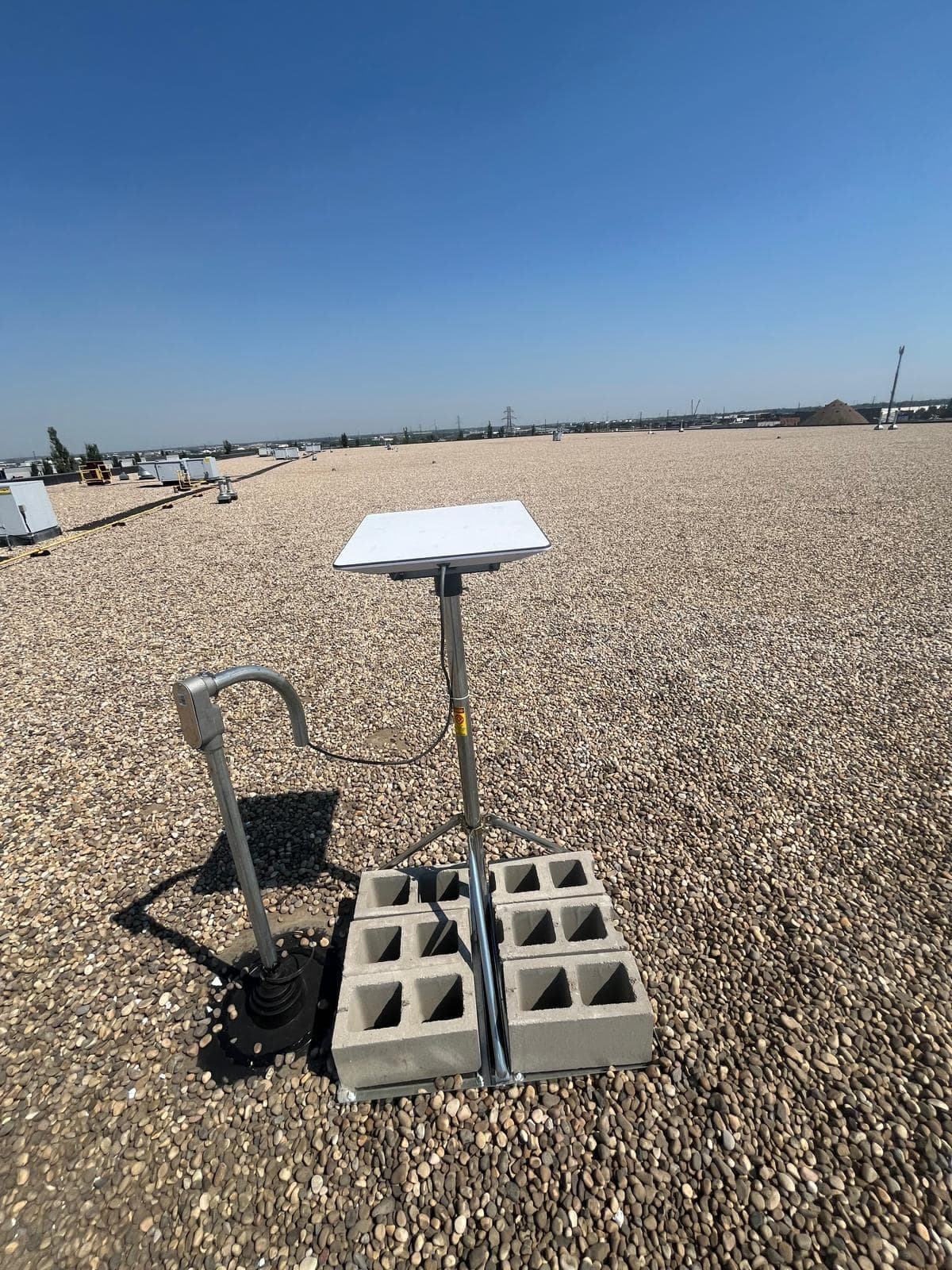 Starlink dish on a ballasted tripod beside a conduit riser sealed with a rubber pipe boot on a gravel roof