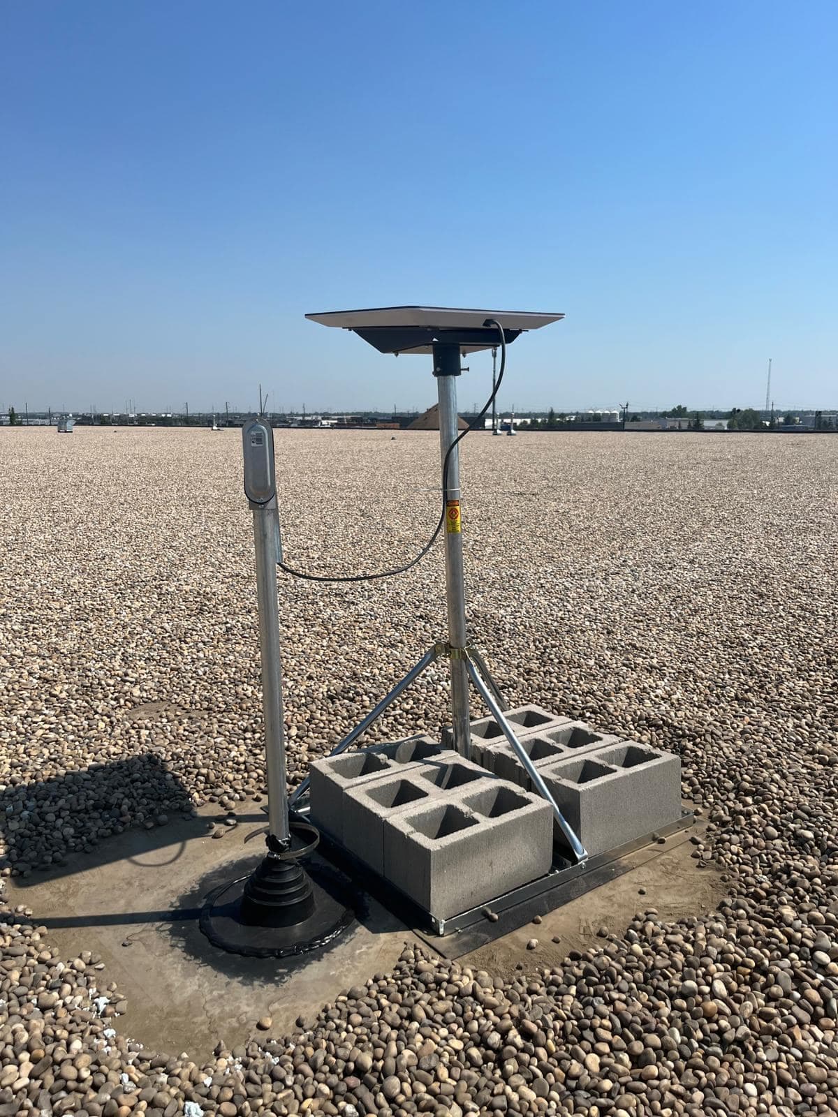 Starlink dish on a galvanised tripod mount weighted with concrete blocks, on a gravel-ballasted commercial flat roof