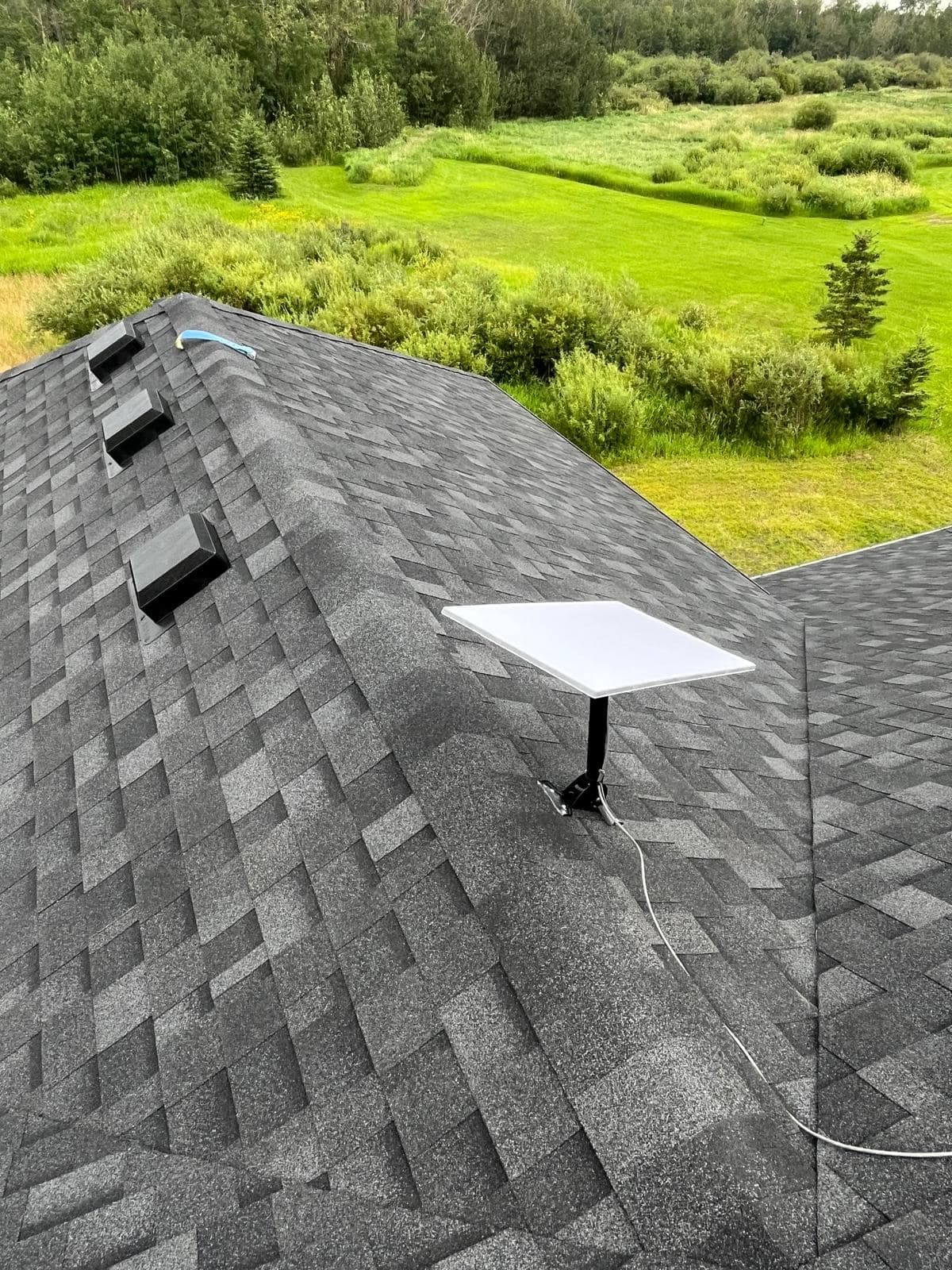 Aerial view of a Starlink dish installed on an asphalt shingle roof, with mown lawn and dense bush beyond