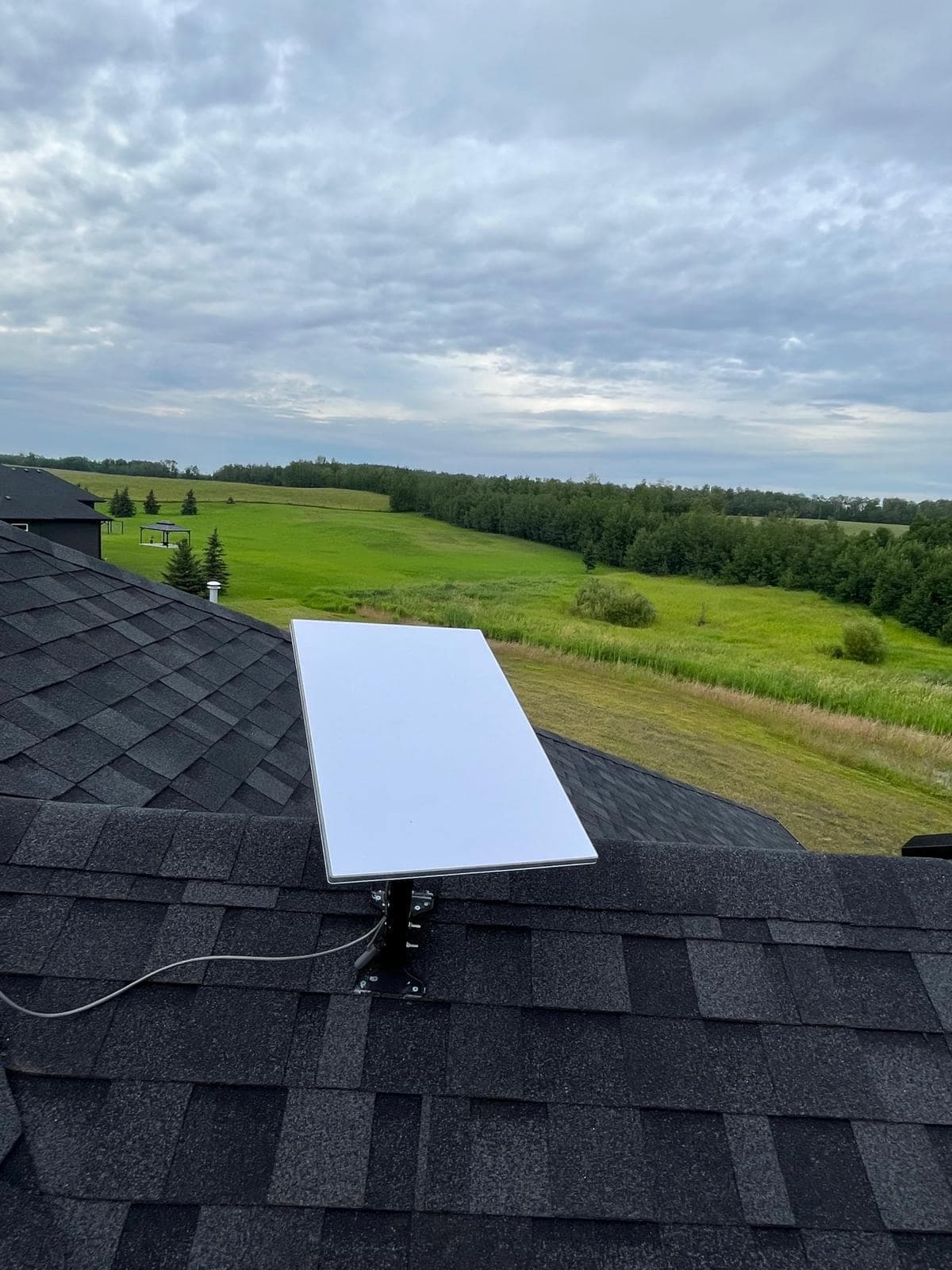 Starlink dish mounted on a roof ridge with a neighbouring property and rolling pasture visible beyond