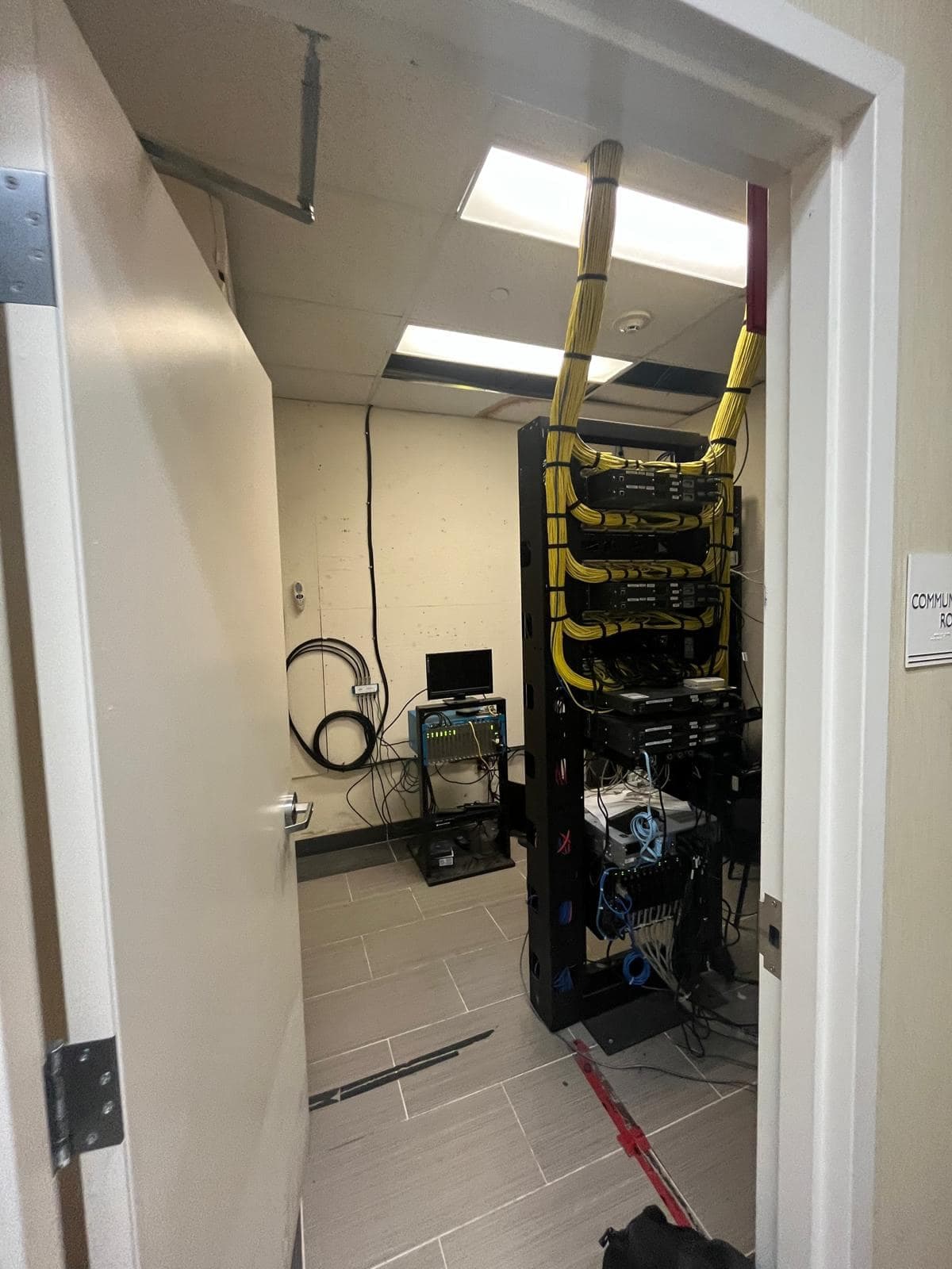 Communications room with an open-frame rack, bundled yellow Cat6 cabling dressed into patch panels, and fibre terminations below